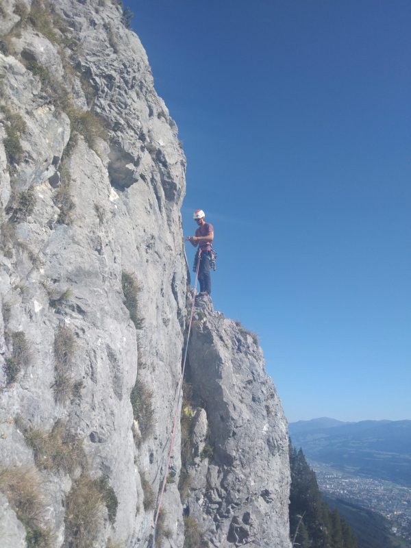 Klettern an der Martinswand. Eine Person steht auf einem Felsvorsprung. Im Hintergrund sieht man das Inntal und Innsbruck